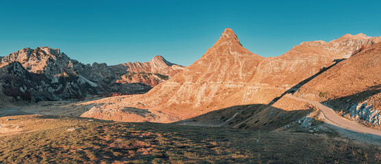 Wall Mural - Golden hour sunlight bathes Sedlo pass in Durmitor national park, Montenegro, highlighting the rugged mountain peaks and creating a dramatic landscape