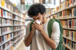 © Cupcake - A student stands in a library, holds his nose and sneezes into a paper napkin. concept of illness flu, disease, allergy, virus,