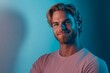 © Maelgoa - A tall, lean man in his late 30s standing with a relaxed pose, smiling into the camera with blond hair and a beard, in a soft blue void, illuminated with soft lighting 2