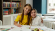 © Yuliia - Happy little girls pretty schoolgirls pupils school students friends sisters classmates children kids hug embrace classroom education studying together learn study smiling looking at camera friendship
