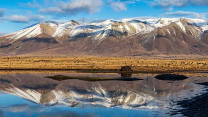 Wall Mural - Reflections  on a rural and remote country water hole in arid tundra desert land near snow capped mountains