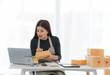 © Kritdanai - Focused Online Business Owner:  A young woman meticulously checks orders at her desk, surrounded by parcels and using a laptop.  She displays concentration and dedication to her e-commerce venture.