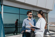 © qunica.com - Two business people engage in a conversation while standing on a high-rise balcony, enjoying a clear day. The modern building reflects an urban environment, fostering an atmosphere of professional