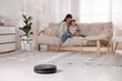 © New Africa - Mother spending time with her daughter in room, focus on robotic vacuum cleaner