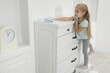 © New Africa - Little helper. Cute girl wiping dust from chest of drawers at home