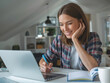 © Leonardo - Mujer joven con una computadora portátil sentada en un escritorio. Ella está escribiendo notas mientras mira un seminario web. La mujer está estudiando en línea, aprendiendo clases web o teniendo una