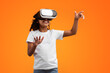 © Prostock-studio - Virtual Reality Concept. Portrait of excited African American girl in VR headset touching air at yellow studio, copy space. Positive teen exploring artificial computer world or playing video game