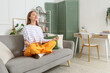 © Pixel-Shot - Young woman meditating on grey couch at home