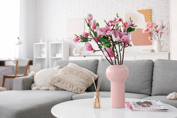 Canvas Print - Vase with beautiful magnolia flowers and magazines on table near grey sofa in modern living room