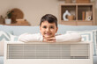 © Pixel-Shot - Cute boy with electric convector heater at home