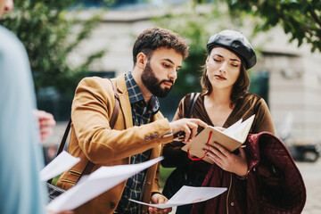 Canvas Print - Two business professionals examine documents and take notes on a project while standing outside. The scene suggests teamwork and collaboration in a strategic business discussion.