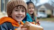 © maesarin - Cheerful children a boy and a girl bundled up in warm winter clothing playing and smiling together in a snowy outdoor setting with a residential house and trees in the background