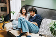 © qunica.com - A young couple sits comfortably on a couch, enjoying a relaxing afternoon reading together. The cozy home setting includes stylish decor and indoor plants, enhancing the peaceful and intimate