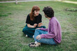 © qunica.com - A young couple is sitting on the grass in casual attire, engaged in a happy conversation in a park setting. The image conveys friendship, relaxation, and connection outdoors.