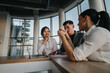© qunica.com - Business professionals engaged in a strategic discussion around a table in a contemporary office with large windows. The team appears focused and collaborative, highlighting teamwork and communication