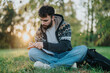 © qunica.com - A bearded man seated on grass writes in a notebook during a tranquil sunset. The serene outdoor setting features lush greenery, offering an atmosphere perfect for reflection and creativity.