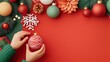 © IceSiCool Studio - Christmas decorations relevance concept. Festive decorations and hands preparing a Christmas ornament on a red background.