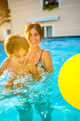 Mother and son having fun, splashing in swimming pool during summer vacation