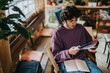 © qunica.com - A young man with curly hair is intently reading a magazine while sitting in a warm and inviting coffee shop. The casual atmosphere suggests relaxation and focus amidst the cozy surroundings.