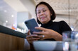 © Johnér - Mid adult woman using mobile phone while sitting in restaurant