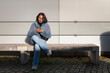 © Johnér - Full length of mid adult woman using mobile phone while sitting against gray wall