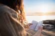 © Johnér - Midsection of woman reading book at lakeshore