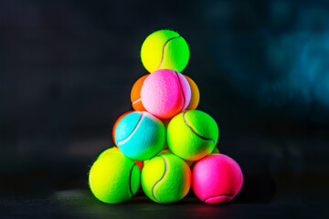 Wall Mural - Pyramid of vibrant neon-colored tennis balls stacked against dark background creates striking contrast and playful energy. Concept of sports, equipment, creativity, and dynamic modern design