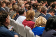 © Anton Gvozdikov - People sitting in chairs at a conference, attentively listening to speakers and presentations.