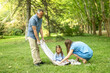 © luisrojasstock - Parents wrapping daughter in blanket in park during summer day