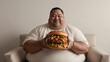 © Olena Yefremkina - Man proudly holds a large hamburger while seated in a softly lit minimalist setting
