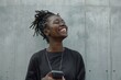 © darshika - Portrait of laughing young african american woman with mobile phone standing against a gray wall