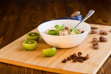 Wall Mural - cooked oatmeal with kiwi, honey and nuts in a bowl on a wooden table