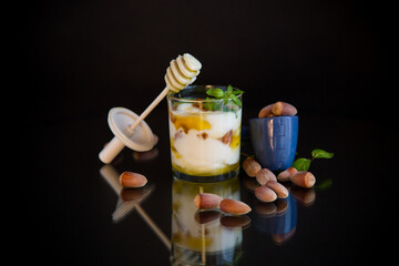 Wall Mural - homemade yogurt with kiwi, honey and nuts in a glass, isolated on black background