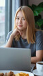 © Flash - A young Asian woman with shoulder-length blonde hair sits at a cafe table, using a laptop, with a cup of coffee.