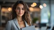 © kaiserseeing - Confident Young Woman in Professional Attire Holding a Laptop in a Modern Office Environment with Blurred Office Background and Warm Lighting