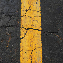 Wall Mural - Cracked yellow line on asphalt road surface creating an aged and worn appearance