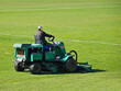 © Xato Lux - Worker on a large green lawn mower mows the grass on the football field. Landscape design and maintenance of green areas of the sports complex. Making grass stadium before the match. Human labor