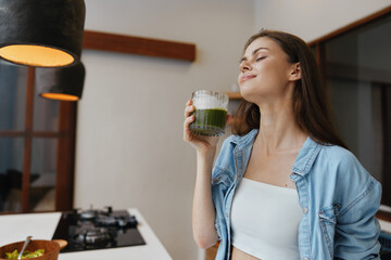 Canvas Print - Young woman enjoying a green smoothie in a modern kitchen, reflecting a healthy lifestyle and positivity with a cozy atmosphere