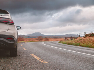 Fototapete - White color family car parked off small narrow road on a bend. Beautiful rough landscape with fields and mountains in the background. Travel in rented car concept. Sightseeing in Connemara, Ireland.