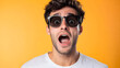 © mahamad - A young man wearing sunglasses, surprised and shocked against an isolated background.