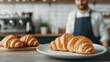 © Arfa_Media - Freshly baked croissants taking center stage in cozy coffee shop, barista brewing in background