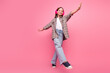 © deagreez - Young girl smiling and posing against pink background while enjoying music with headphones in a trendy casual outfit.