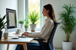 © miss irine - Young woman sits at modern office desk. Keeps good posture working on computer. Indoor office setting. Plants visible. Focus on comfortable work environment, productivity. Modern office scene.