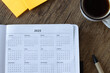 © Marinela - 2025 calendar year in notebook planner on wooden desk with coffee cup and sticky notes. Top view. Annual goals, budget, aspirations, monthly schedule concept.