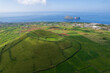 © aroxopt - Aerial view of Terceira islans in Azores, Portugal. Volcanic landscape.  Drone shot of ancient Pico Dona Joana volcano and  cabras islet. Green fields in rural environment.