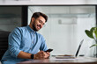 © insta_photos - Busy happy young Latin business man holding smartphone sitting in office. Professional hispanic businessman entrepreneur or manager using financial banking apps on cell mobile phone technology at work