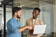 © insta_photos - Business team of two busy happy professional business men employees working together standing in corporate office having conversation sharing ideas using laptop computer technology.