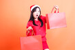 © Ajab - Asian woman beauty wearing red blouse and santa hat, standing sideways to left surprised to camera both hands holding red bag of christmas gifts up and down, isolated on white background