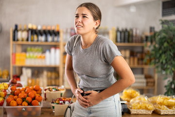 Wall Mural - Young woman buyer with abdominal pain in grocery store