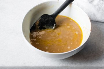 Canvas Print - Overhead view of Mixing Melted butter and Madeleine batter in a white mixing bowl, process of making madeleines